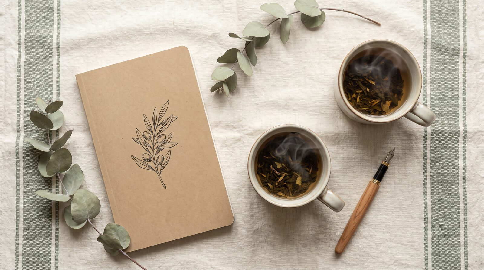 Flat lay of a botanical planner, herbal tea, and pen on linen fabric